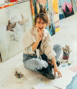 Happy female artist sitting on studio floor with art
