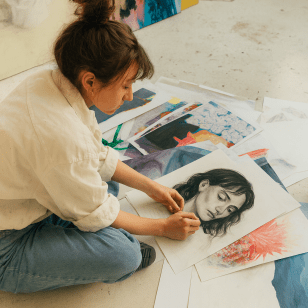A female artist sits on the ground looking through a collection of drawings