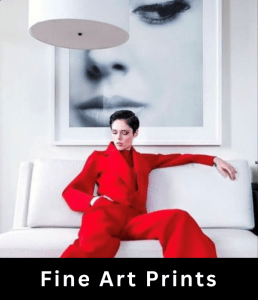 Female model with dark hair and wearing red jacket and pants, sits on a sofa in front of a large fine art print