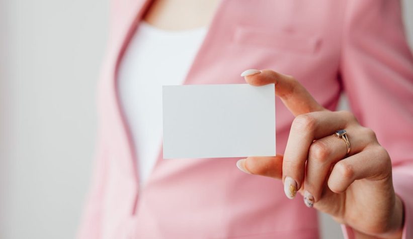 Photograph of woman wearing a pink suit, holding a business card