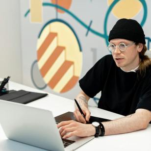 Male artist sits at desk with laptop designing his website