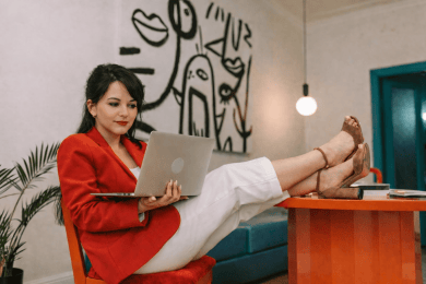 Young woman wearing red jacket sits at desk with laptop