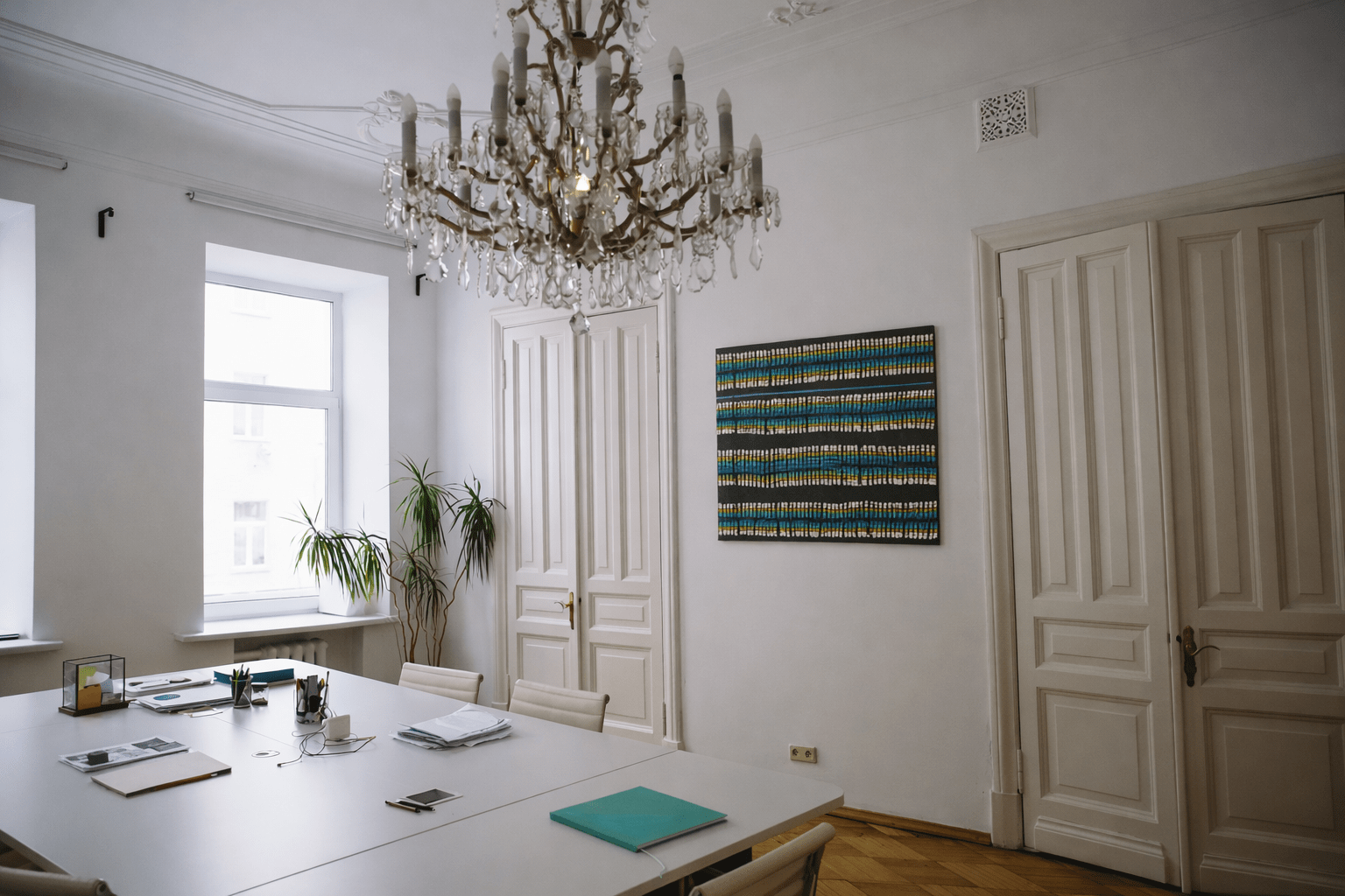 Meeting room with chandelier and white walls featuring Saltwater Country by Anthony J. Walker (Yiman, Ghungalu, Gooreng Gooreng peoples of Central Queensland), a 24.4 × 18 inch Indigenous Australian artwork with turquoise, blue, white and yellow dot patterns on black.