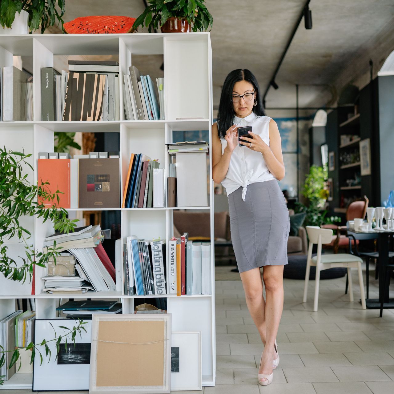Young woman stands beside bookshelf