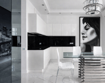 Modern white kitchen with black marble accents and a glass dining table; a large floor‑to‑ceiling framed monochrome portrait of a woman in profile (Victoria) adds a dramatic focal point on the right‑hand wall, harmonizing with the room’s minimalist palette and reflective surfaces.